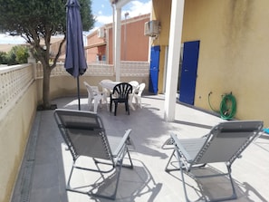 Eine Terrasse mit Gartenmöbeln, einer blauen Tür und einer Klimaanlage.
