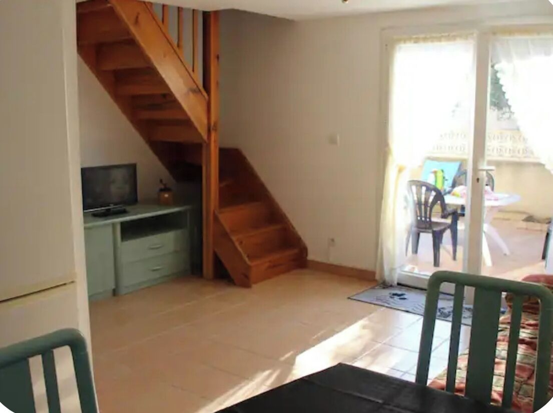 A room with a wooden staircase, a desk, a chair, and a sliding glass door leading to an outdoor area.