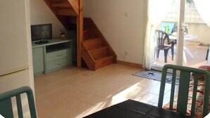 Una habitación con escalera de madera, un escritorio, una silla y un ventanal corredera que da a un espacio exterior.