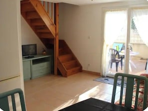 Ein Zimmer mit einer Holztreppe, einem Schreibtisch, einem Stuhl und einer Glastür zum Außenbereich.