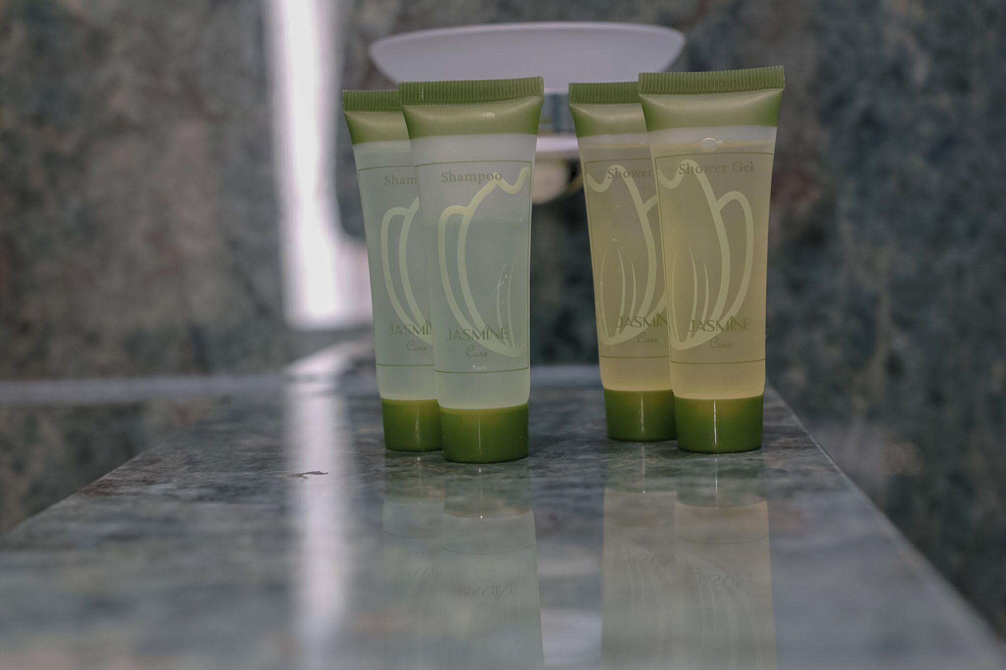 Three tubes of jasmine shower gel on a marble countertop.