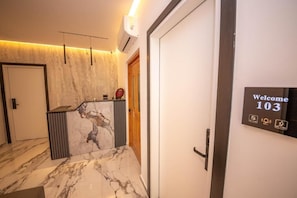 Una zona de recepción con mostrador de mármol, un cartel de bienvenida y una puerta con picaporte.