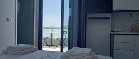 Une chambre à coucher avec un lit, une petite table et une vue sur la mer, visible à travers une porte vitrée.
