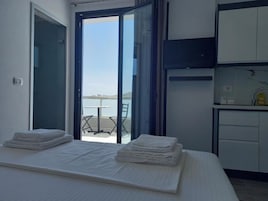 Une chambre à coucher avec un lit, une petite table et une vue sur la mer, visible à travers une porte vitrée.