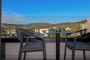 Un balcón con dos sillas y una mesa, con vistas a un paisaje montañoso y edificios a la distancia.