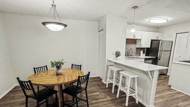 A modern kitchen with white cabinets, a stainless steel refrigerator, and a wooden dining table with chairs. - Quiet & Relaxing 2BR - King Bed/Pool/Gym Near UAB/Hospitals (Homewood)