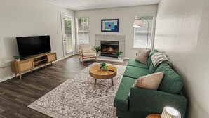A living room with a green sofa, a flat-screen TV, a fireplace, and a patterned rug. - Quiet & Relaxing 2BR - King Bed/Pool/Gym Near UAB/Hospitals (Homewood)