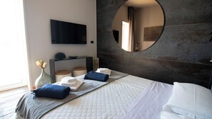 Ein modernes Hotelzimmer mit einem großen Bett, einem Flachbildfernseher, einem runden Spiegel und einem kleinen Nachttisch mit einer Vase.