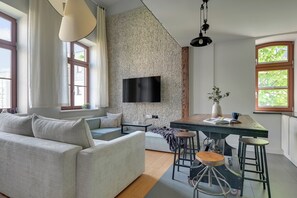 Een moderne woonkamer met een bank, een eettafel met krukken, een flatscreen-tv bevestigd aan een structuurrijke muur en grote ramen.