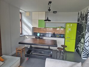 Eine moderne Küche mit einem Holztisch, Hockern, einem grünen Kühlschrank und einer Stadtlandschaftsmalerei.