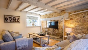 Un salon chaleureux avec des murs en pierre, un téléviseur à écran plat fixé au mur, une table basse en bois et des sièges confortables.