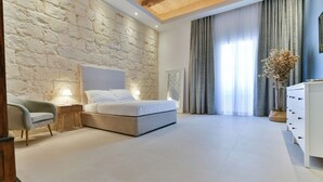 Een slaapkamer met een stenen muur, een bed, een nachtkastje, een dressoir en een raam met gordijnen.