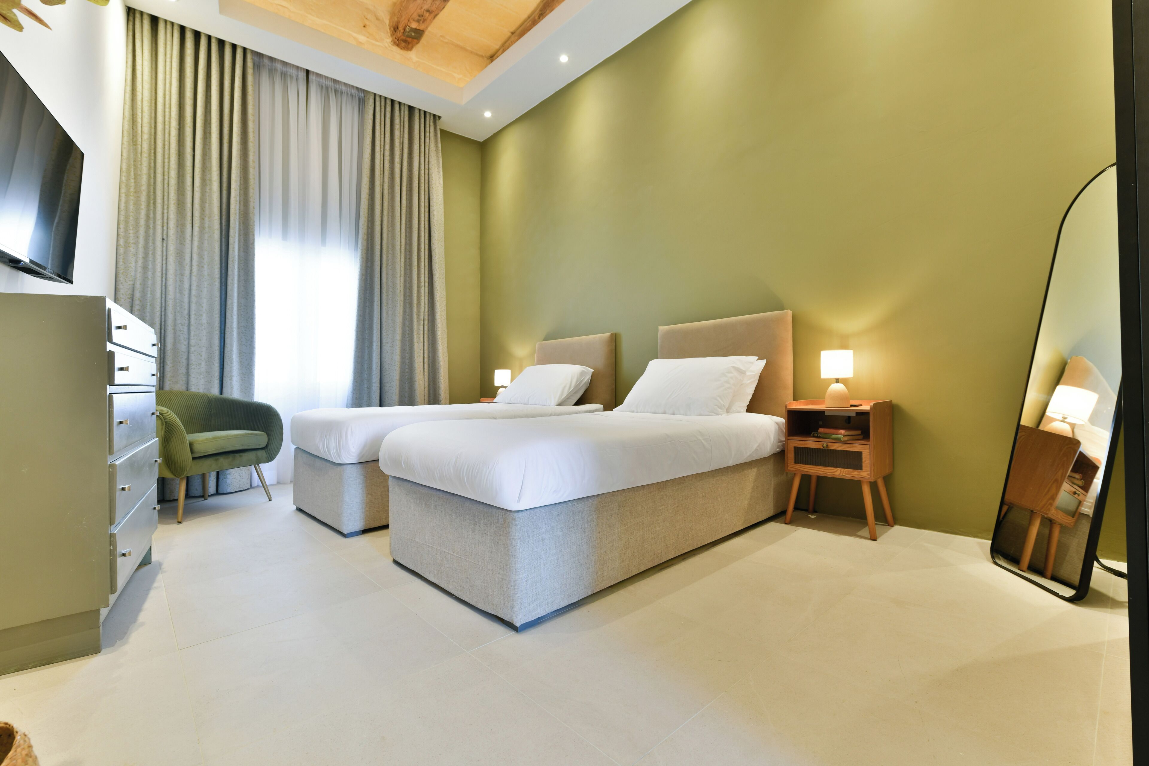 A modern hotel room with a bed, a desk, a chair, and a mirror.