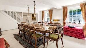 A dining room with a wooden table set for six, surrounded by chairs with green cushions.