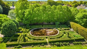 Un giardino formale con uno stagno centrale, siepi curate e diverse specie di alberi.