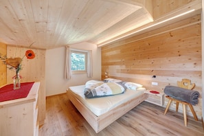 Una habitación de cabaña de madera con una cama, una mesita, una silla y una ventana.