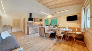 A modern interior with a wooden floor, a dining area with a table and chairs, a kitchen with wooden cabinets, and a TV mounted on the wall. - Apartment 'Marschalkhof Peilstein' with Mountain View, Shared Garden and Wi-Fi (San Pancrazio)