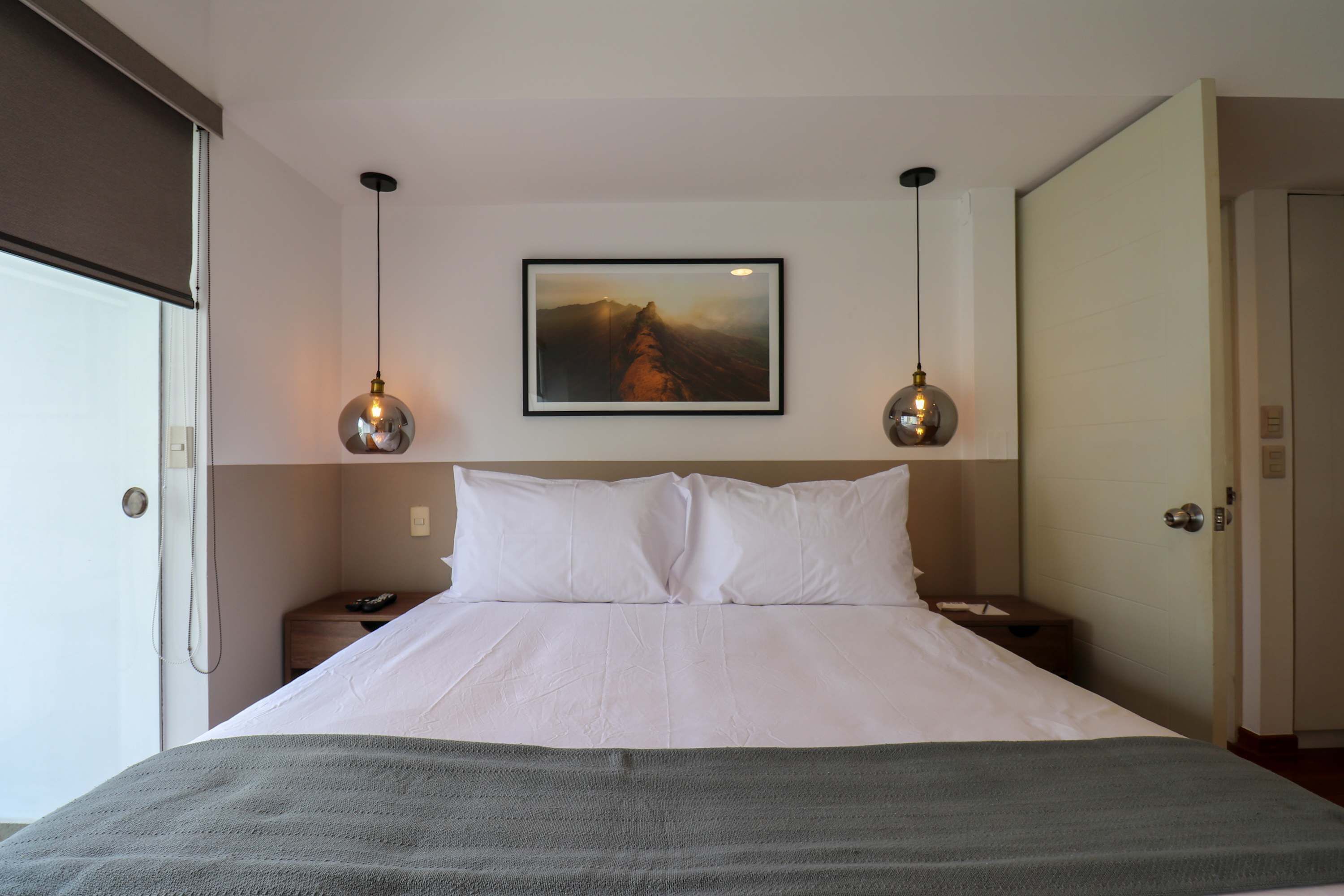 Une chambre d’hôtel avec un grand lit, deux tables de chevet, un tableau au mur et deux lampes suspendues.