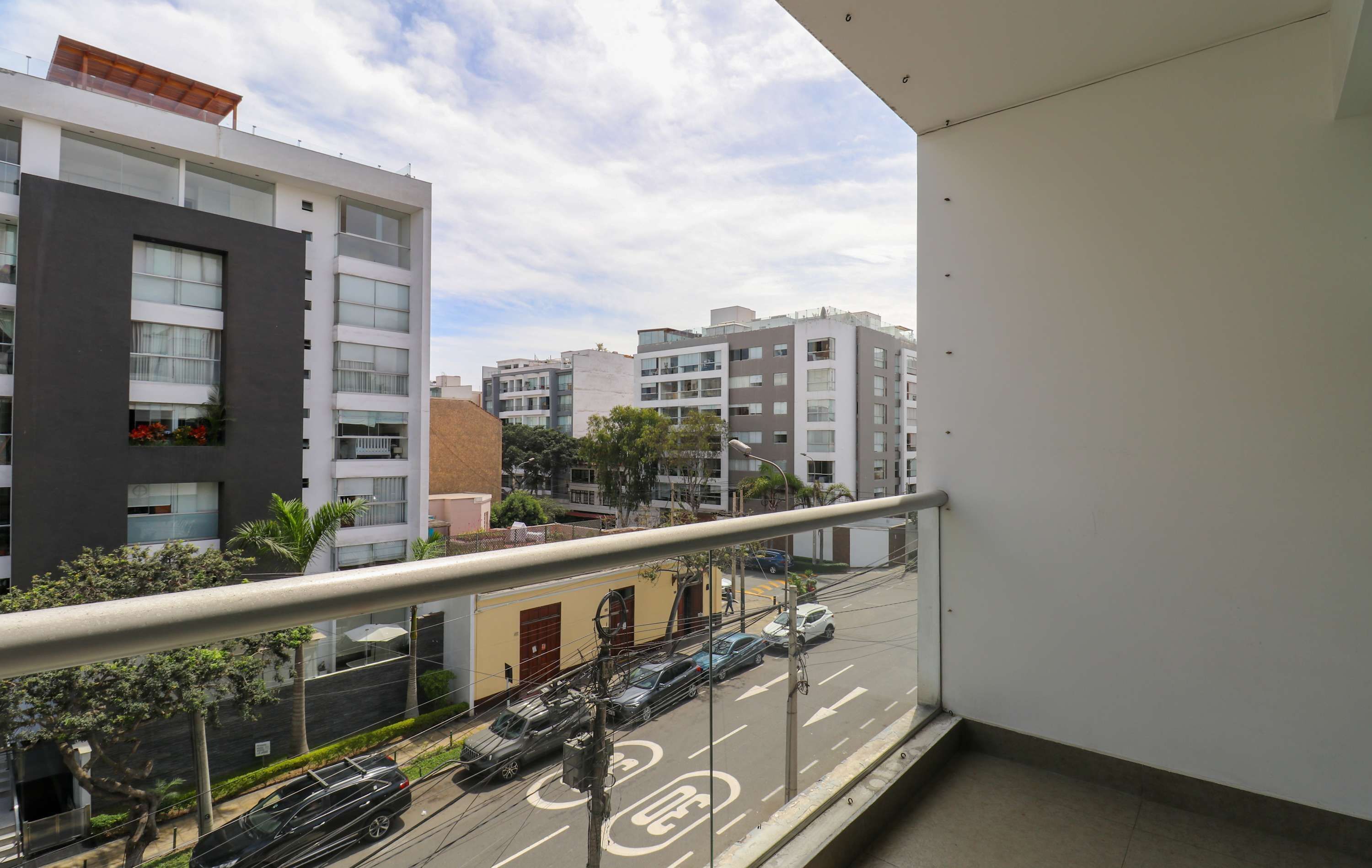 En balkon med udsigt over moderne bygninger, en gade med biler og et fodgængerfelt.