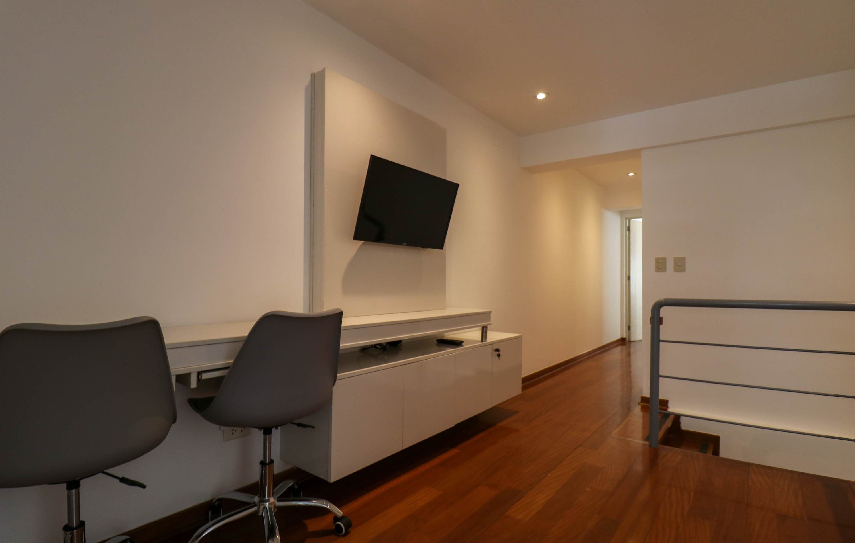 A modern hotel room with a flat-screen TV mounted on the wall, a wooden floor, and a white console table with two chairs.