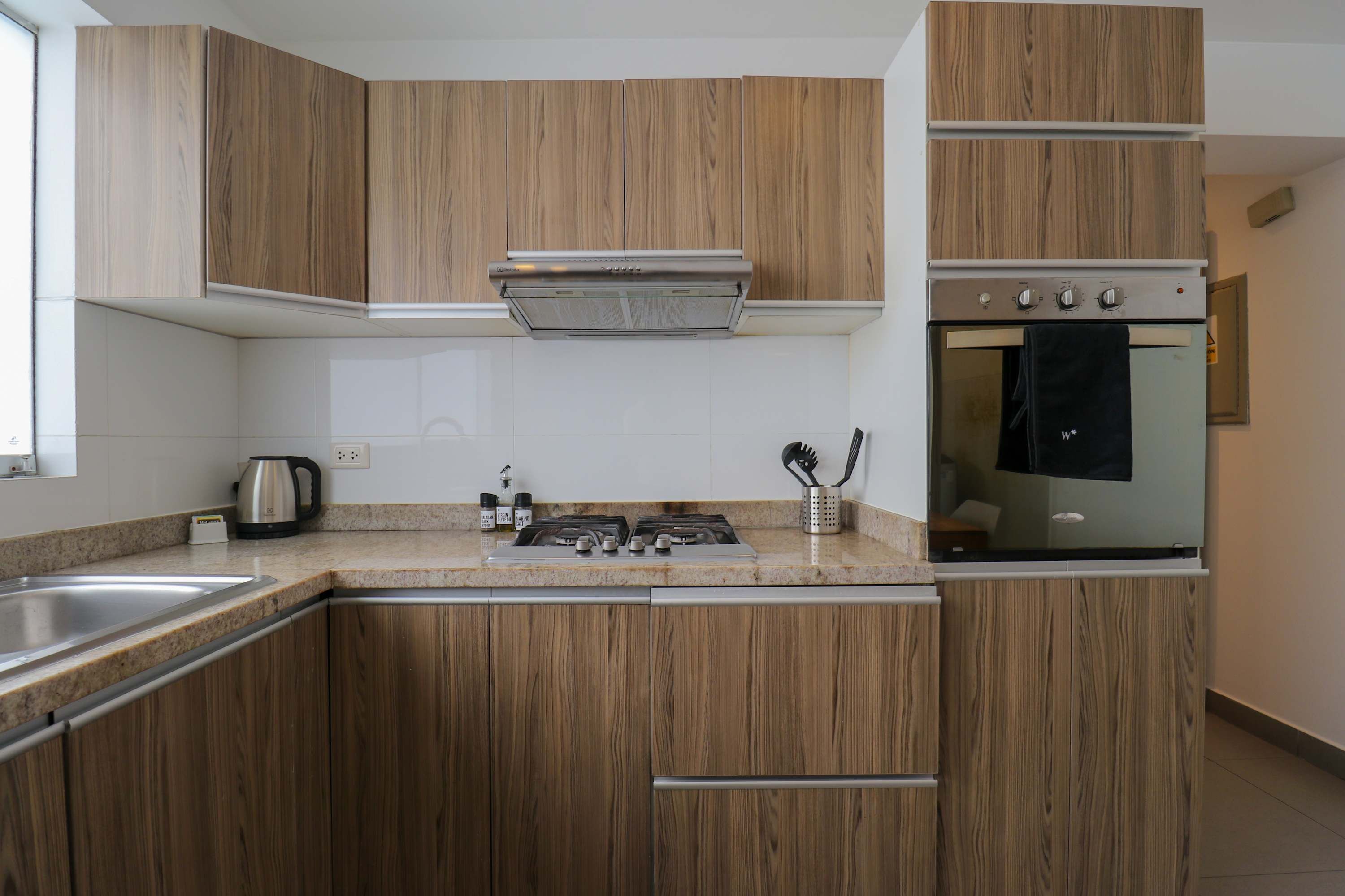 Una cucina moderna con mobili in legno, una cappa in acciaio inossidabile, forno integrato e lavello.