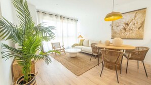 Un salon comprenant un canapé, une table basse, une table à manger, des chaises, une plante en pot et un tableau accroché au mur.