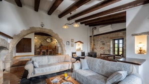 A cozy living room with two patterned sofas, a wooden coffee table, and a stone fireplace. - Altair Blue Villa - Private Jacuzzi and Views (Hersonissos)