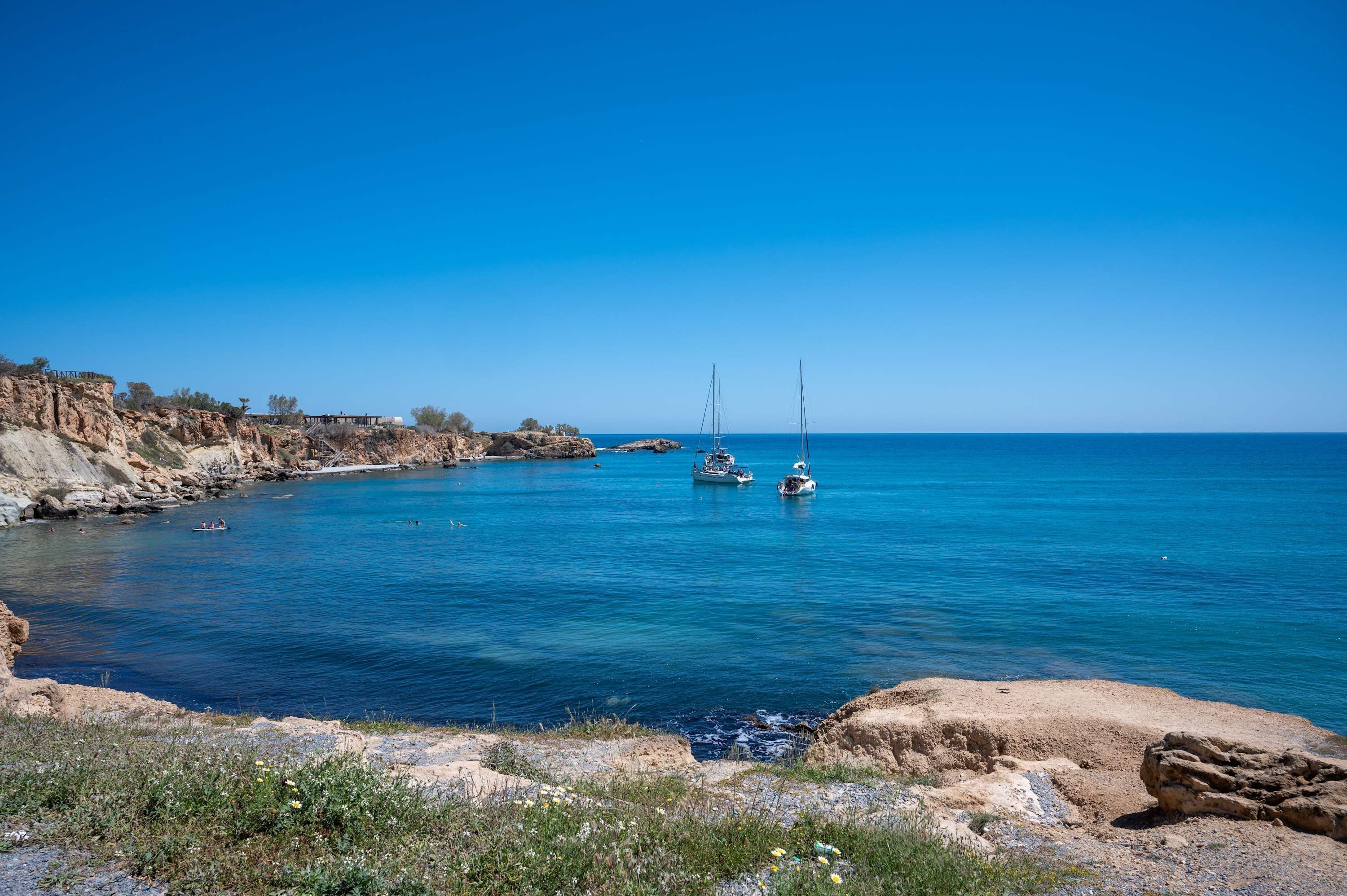 A coastal scene with clear blue water, rocky cliffs, and boats.