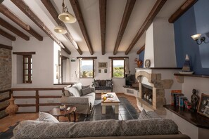 A cozy living room with exposed wooden beams, a stone fireplace, and a view of the outdoors.