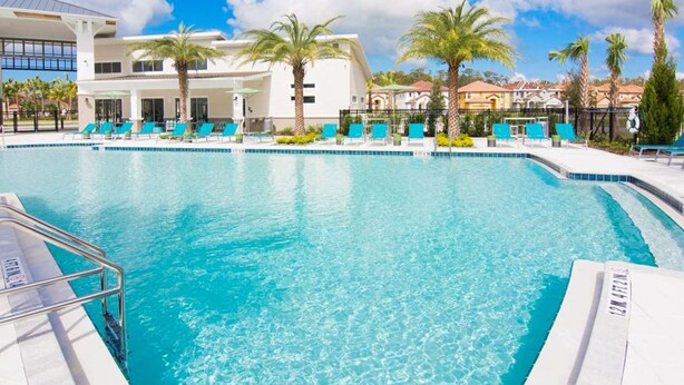 Ein Pool mit Liegestühlen, Palmen und einem Gebäude mit großen Fenstern.