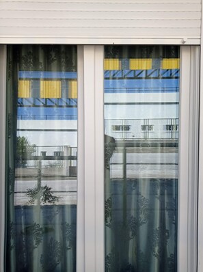 Ein Fenster mit einem gemusterten Vorhang und Blick auf ein Mehrstöckgebäude mit Balkonen.