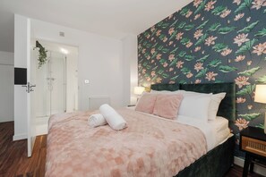 Quarto com cama, mesa de cabeceira, luminária e área de chuveiro.