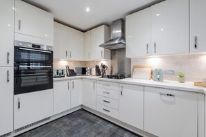 Una cocina moderna con armarios blancos, horno empotrado, campana extractora de acero inoxidable y una encimera con un hervidor y una planta pequeña.