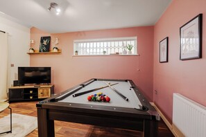Uma mesa de bilhar com bolas, uma televisão e uma janela com plantas.