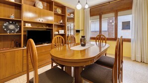 Un coin repas comprenant une table en bois, des chaises, un téléviseur et des étagères où sont rangés divers objets.
