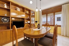 Un comedor con una mesa de madera, sillas, un televisor y estantes con varios objetos.