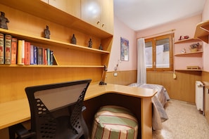 A compact room with a wooden desk, a chair, a bed, a radiator, and shelves with books and figurines. - Apartment 'Can Molone' with Wi-Fi (Cornudella de Montsant)