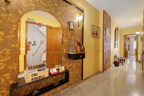 Zona de recepción de hotel con pared de mármol, mostrador de madera, un espejo y un banco en el pasillo.