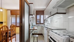 Une cuisine de taille réduite, équipée d’une cuisinière à gaz, d’un évier et de chaises en bois.