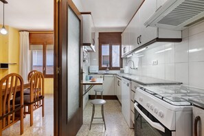 Una cocina compacta con estufa a gas, un lavamanos y sillas de madera.