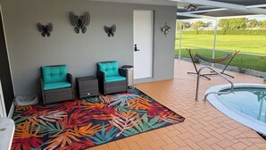 Un espace extérieur abrité avec une piscine, deux fauteuils en osier dotés de coussins turquoise, un tapis aux motifs tropicaux et colorés, et des décorations en forme de papillons fixées au mur.