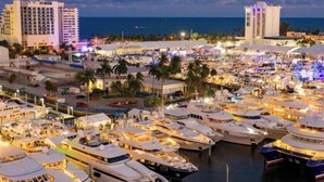 Un port de plaisance où sont amarrés de nombreux yachts, entouré de bâtiments et de palmiers.