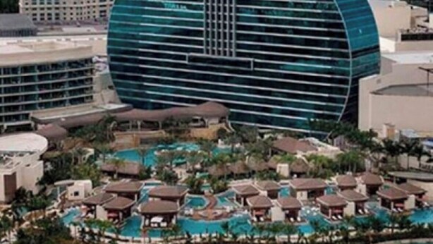 Un grand bâtiment en forme de guitare, entouré d’un complexe hôtelier comprenant des piscines et des villas.