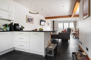 Une cuisine moderne avec des meubles blancs, un plan de travail noir et un coin repas comprenant un canapé gris et une table en bois.