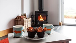 Una habitación acogedora con chimenea, dos tazas decoradas con motivos de zorro y muffins sobre un posavasos.
