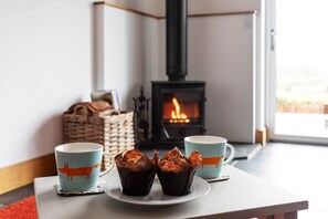 Une pièce chaleureuse avec une cheminée, deux tasses décorées de motifs de renards et des muffins posés sur un dessous de verre.
