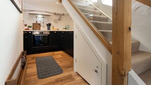 Een keuken met donkere kastjes, een houten trap en een grijze vloerkleed.
