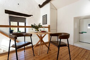 A room with a wooden floor, two leather chairs, a round wooden table, a potted plant, and a framed picture on the wall. - Craftsman's Loft (Hawkshead)