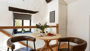 Een eetgedeelte met een ronde houten tafel, twee leren stoelen, een potplant, een fles en een bord met bestek.