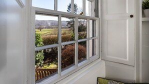Una ventana con vistas a un jardín y colinas lejanas.